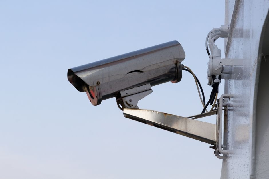 Gros plan sur un détecteur de mouvement extérieur fixé sur un mur de maison européenne, surveillant un jardin avec végétation